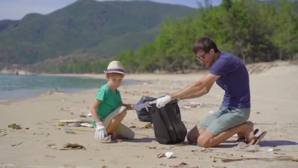 Een man en een jongen in handschoenen verzamelen plastic afval op een strand. Het probleem van afval op het strand zand veroorzaakt door door door de mens veroorzaakte vervuiling. Eco-campagnes om het milieu te reinigen. Ecologisch vrijwilligerswerk — Stockvideo