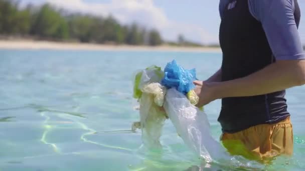 Colpo palmare di un uomo che raccoglie sacchetti di plastica nel bellissimo mare turchese. Paradiso inquinamento spiaggia. Il problema della spazzatura sulla sabbia della spiaggia causata dall'inquinamento causato dall'uomo. Campagne ecologiche — Video Stock