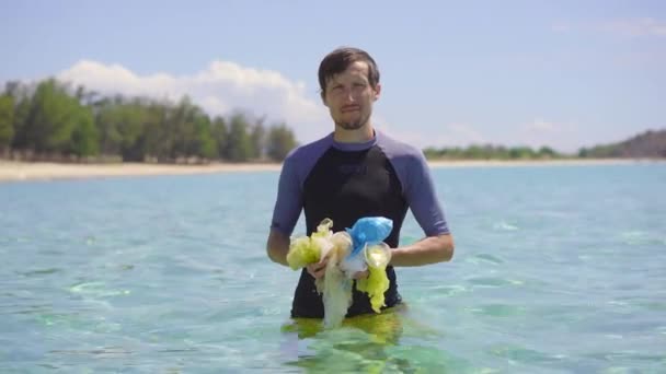 Ręczne ujęcie mężczyzny, który zbiera plastikowe torby w pięknym turkusowym morzu. Rajskie zanieczyszczenie plaży. Problem śmieci na piasku plażowym spowodowany zanieczyszczeniem spowodowanym przez człowieka. Kampanie ekologiczne na rzecz — Wideo stockowe