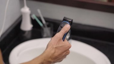 Sakalını sakal kesme makinesiyle kesen genç bir adamın yakın plan fotoğrafı.
