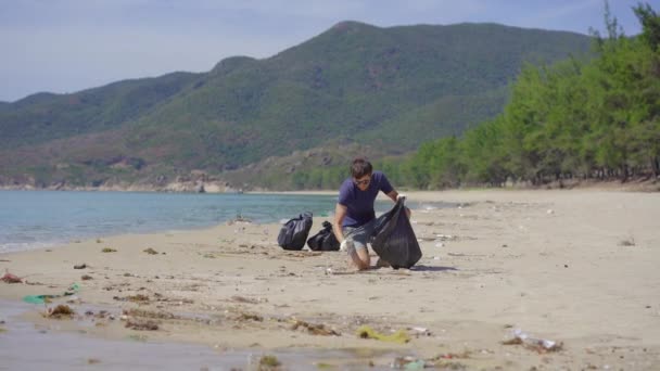 Человек в перчатках собирает пластиковый мусор на пляже. Проблема мусора на пляжном песке, вызванного техногенным загрязнением. Эко-кампании по очистке окружающей среды. Концепция экологического волонтерства — стоковое видео