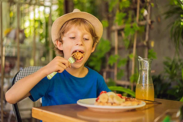 Мальчик ест бельгийские вафли с клубникой в кафе — стоковое фото