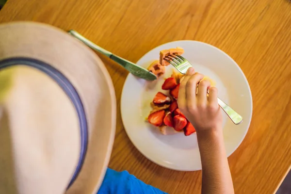 Un ragazzino mangia il dessert waffle belgi con fragola in un caffè — Foto Stock