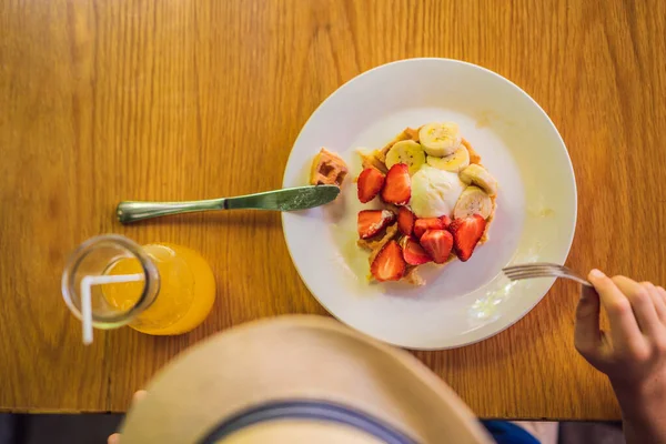 Um menino come sobremesa waffles belgas com morango em um café — Fotografia de Stock