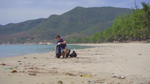Man in gloves collects plastic trash on a beach. The problem of garbage on the beach sand caused by man-made pollution. Eco campaigns to clean the environment. Ecological volunteering concept — Stock Video