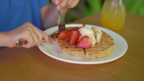 Um garotinho come sobremesa waffles belgas com morango e gelado em um café — Vídeo de Stock