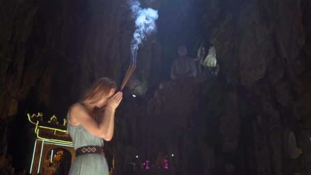 Una giovane donna europea sta pregando tenendo in mano dei bastoncini di aroma fumante. Lei è nel più grande tempio delle caverne nelle montagne di marmo un complesso di templi buddisti, una famosa destinazione turistica in — Video Stock