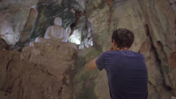 Mladý Evropan se modlí, aby držel v rukou kouřící vonné tyčinky. Je v největším jeskynním chrámu v mramorových horách komplexem buddhistických chrámů, známým turistickým cílem v — Stock video