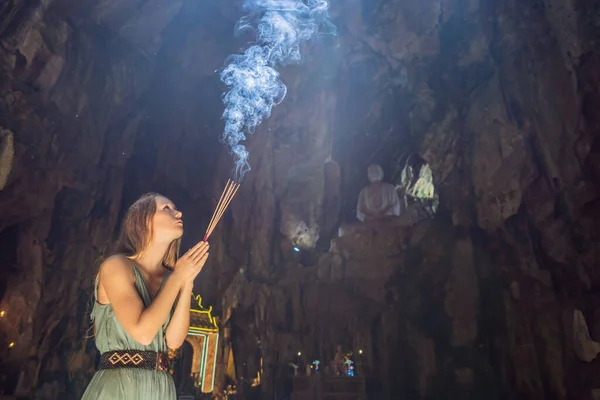 Молодая женщина молится в буддийском храме, держа ладан в пещере Хюйен Кхонг с святынями, Мраморные горы, Вьетнам — стоковое фото