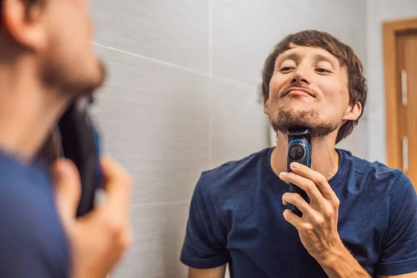 Handsome young bearded man trimming his beard with a trimmer — Stock Photo, Image