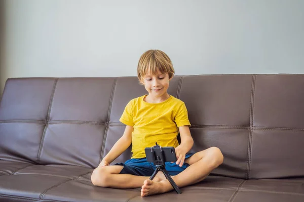 Zůstávám ve spojení. Šťastný mladý chlapec se dívá na svůj mobilní telefon a usmívá se při hraní s hračkami. Chlapec mluví s někým přes video komunikaci během vlastní izolace kvůli karanténě COVID 19 — Stock fotografie