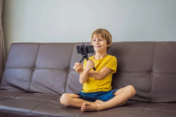 Zůstávám ve spojení. Šťastný mladý chlapec se dívá na svůj mobilní telefon a usmívá se při hraní s hračkami. Chlapec mluví s někým přes video komunikaci během vlastní izolace kvůli karanténě COVID 19 — Stock fotografie