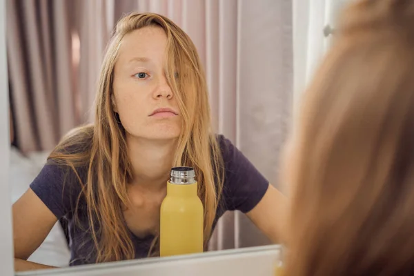 Очень усталая молодая женщина смотрит на себя в зеркало, дома одна. самоизоляция дома, карантин из-за пандемии COVID 19. Проблемы психического здоровья в самоизоляции дома — стоковое фото