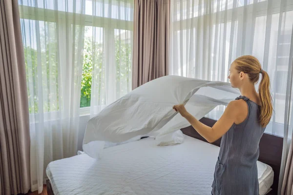 Young Female Housekeeper Changing Bedding In Hotel Room