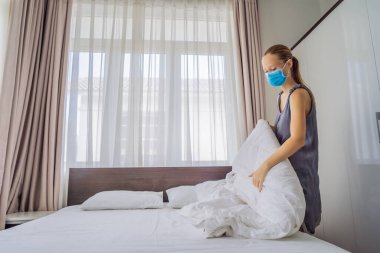 Coronavirüs karantinası nedeniyle tıbbi maske takan genç kadın hizmetçi COVID 19 Değişen Yatak Odası