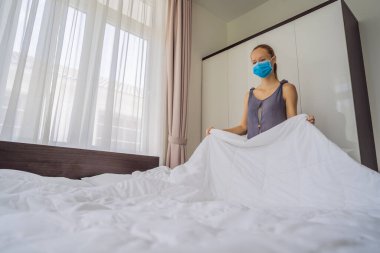 Coronavirüs karantinası nedeniyle tıbbi maske takan genç kadın hizmetçi COVID 19 Değişen Yatak Odası