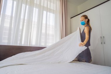 Coronavirüs karantinası nedeniyle tıbbi maske takan genç kadın hizmetçi COVID 19 Değişen Yatak Odası