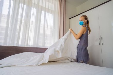 Coronavirüs karantinası nedeniyle tıbbi maske takan genç kadın hizmetçi COVID 19 Değişen Yatak Odası