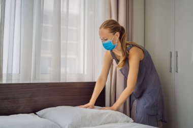 Coronavirüs karantinası nedeniyle tıbbi maske takan genç kadın hizmetçi COVID 19 Değişen Yatak Odası