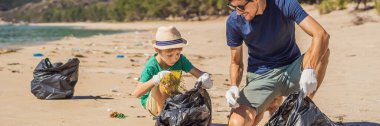 Plajı temizleyen eldivenli baba ve oğul kirli denizi temizleyen plastik torbaları topluyorlar. Çocukların doğal eğitimi. İnsan yapımı kumsalda dökülen çöplerle ilgili bir sorun.