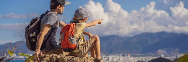 Father and son local tourist sits on a rock and enjoys the view of her city. Local tourism concept. Tourism after COVID 19 BANNER, LONG FORMAT — Stock Photo, Image