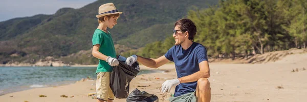 Папа и сын в перчатках убирают на пляже пластиковые пакеты, которые загрязняют море. Естественное воспитание детей. Проблема высыпания мусора на пляжный песок, вызванного техногенной деятельностью — стоковое фото