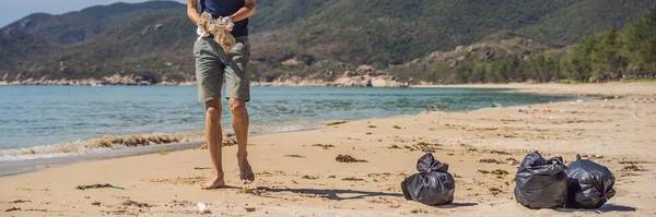Ο άντρας με τα γάντια μαζεύει πλαστικές σακούλες που μολύνουν τη θάλασσα. Πρόβλημα χύνονται σκουπίδια σκουπίδια σκουπίδια στην άμμο παραλία που προκαλείται από την ανθρωπογενή ρύπανση και το περιβάλλον, εκστρατεία για να καθαρίσει εθελοντής στην έννοια — Φωτογραφία Αρχείου