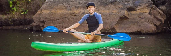 Ein fröhlicher Mann trainiert an einem sonnigen Morgen im Fluss SUP-Board. Stand-up-Paddle-Boarding - tolle aktive Outdoor-Erholung BANNER, LONG FORMAT — Stockfoto