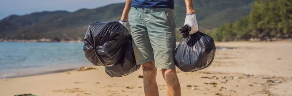 El hombre con guantes recoge bolsas de plástico que contaminan el mar. Problema de la basura derramada basura basura en la playa arena causada por la contaminación causada por el hombre y el medio ambiente, campaña para limpiar el voluntariado en concepto — Foto de Stock