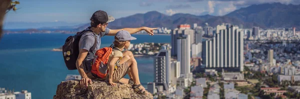 Baba ve oğul yerel turist bir kayanın üzerinde oturuyor ve şehrin manzarasının tadını çıkarıyor. Yerel turizm konsepti. COVID 19 BANNER 'dan sonra turizm — Stok fotoğraf