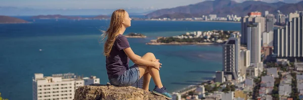 Een jonge vrouw lokale toerist zit op een rots en geniet van het uitzicht op haar stad. Lokaal toeristisch concept. Toerisme na COVID 19 BANNER, LANG FORMAT — Stockfoto