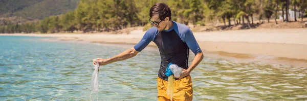 Мужчина собирает пакеты из красивого бирюзового моря. Райское загрязнение пляжа. Проблема высыпания мусора мусора на пляжный песок, вызванного техногенным загрязнением и окружающей средой, кампания по — стоковое фото