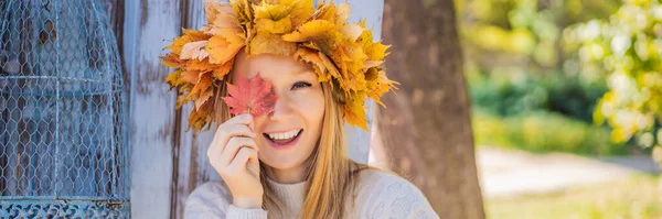 秋の葉のリースを身に着けている魅力的なブロンドの若い女性の屋外ライフスタイルのクローズアップ肖像画。スタイリッシュなニットプルオーバーを身に着けている。メープルのリースはバナー、ロングフォーマットを残します — ストック写真