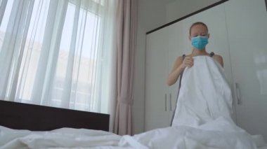 Tıbbi maske takan genç bir kadın otel odasında çarşaf değiştiriyor. Otel yurtdışından gelenler için özel bir karantina tesisi olarak çalışıyor. COVID konsepti sırasında seyahat