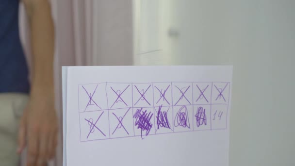 Ein junger Mann in Zwangsquarantäne. Er kreuzt die Nummer 14 im Kalender, den er gezeichnet hat. Er ist glücklich, weil er jetzt die Quarantäne verlassen kann. Konzept der zweiten Welle von Covid-19 — Stockvideo