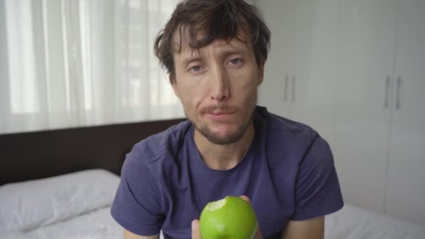 強制隔離された若い男の閉鎖ショット。彼はリンゴを食べる。2週間1つの部屋に滞在し、長い時間のために剃っていない、ヘアカットが必要です。彼は強調され動揺している。概念 — ストック動画