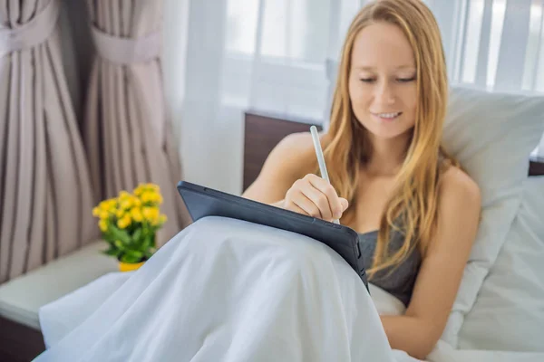 Женщина рисует на скрижали со стилусом в постели — стоковое фото
