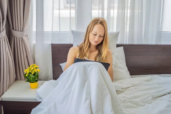 Woman draws on tablet with stylus in bed