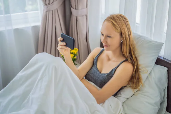 Relaxed woman using a smart phone on the bed at home