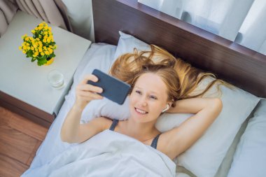 Rahat bir kadın evdeki yatakta akıllı bir telefon kullanıyor.