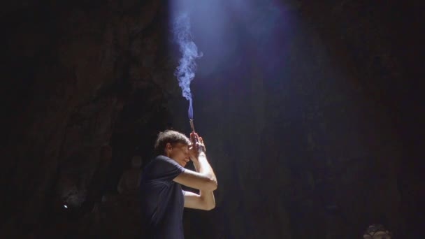 Lassított felvétel egy fiatal európai férfiról, aki azért imádkozik, hogy füstölgő aromát tartson a kezében. A Márvány-hegység legnagyobb barlangtemplomában van, egy buddhista templomkomplexum, egy híres. — Stock videók