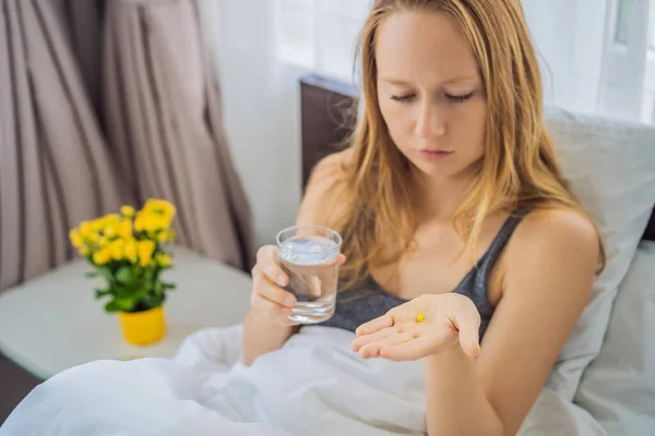 Kobieta cierpiąca na chorobę lub bezsenność leżąca w łóżku i zamierzająca przyjąć tabletkę leku — Zdjęcie stockowe