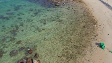 Açık mavi deniz suyunda şnorkelle yüzen genç bir kadının 4K hava görüntüsü.