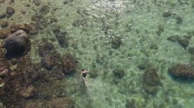 Açık mavi deniz suyunda şnorkelle yüzen genç bir kadının 4K hava görüntüsü.