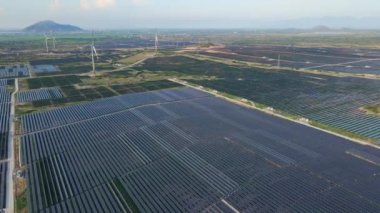 Büyük bir tarlada rüzgar türbinleriyle karıştırılmış devasa bir güneş enerjisi santralinin havadan çekimi. Güneş enerjisi ve rüzgardan elektrik üretimi. Yeşil enerji ve sıfır emisyon kavramı