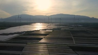 Büyük bir tarlada rüzgar türbinleriyle karıştırılmış devasa bir güneş enerjisi santralinin havadan çekimi. Güneş enerjisi ve rüzgardan elektrik üretimi. Yeşil enerji ve sıfır emisyon kavramı
