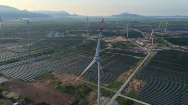 Büyük bir tarlada rüzgar türbinleriyle karıştırılmış devasa bir güneş enerjisi santralinin havadan çekimi. Güneş enerjisi ve rüzgardan elektrik üretimi. Yeşil enerji ve sıfır emisyon kavramı