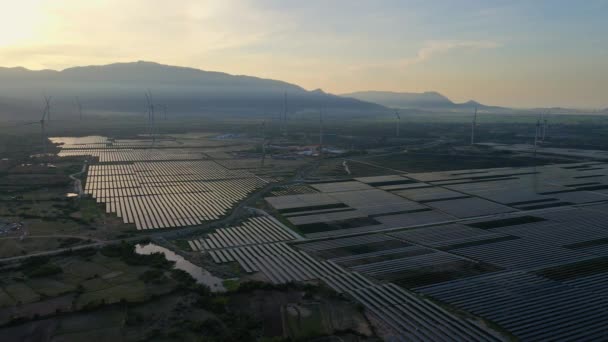 Légi felvétel egy hatalmas naperőműről, szélturbinákkal keverve egy nagy mezőn. Villamosenergia-termelés nap- és szélenergiából. Zöld energia és kibocsátásmentes koncepció — Stock videók