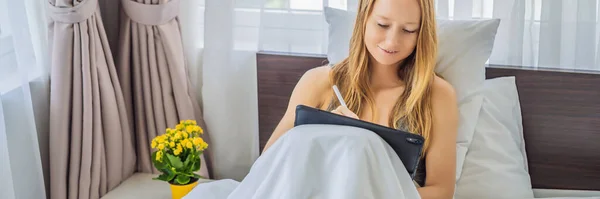 Woman draws on tablet with stylus in bed BANNER, LONG FORMAT