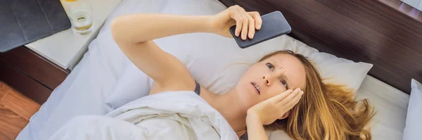 Спящая женщина с удивленным выражением лица, глядя на телефон после того, как пропустила будильник и проснулась поздно. — стоковое фото